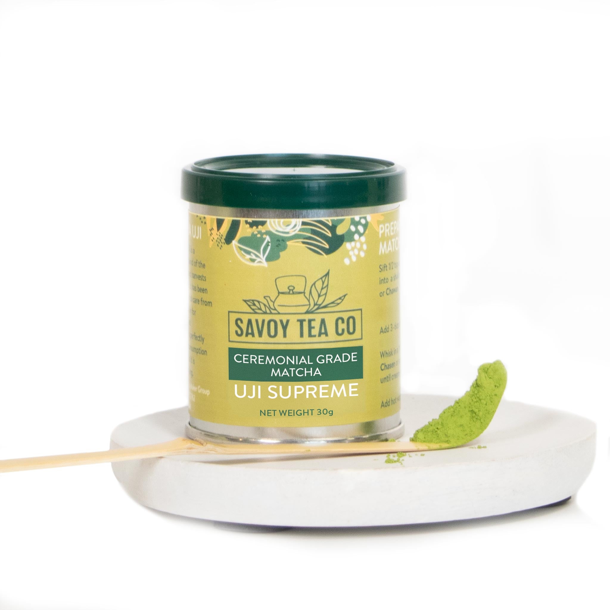 A canister of Savoy Tea Co. ceremonial grade Uji Supreme matcha tea, placed on a white plate with a spoonful of matcha powder next to it.