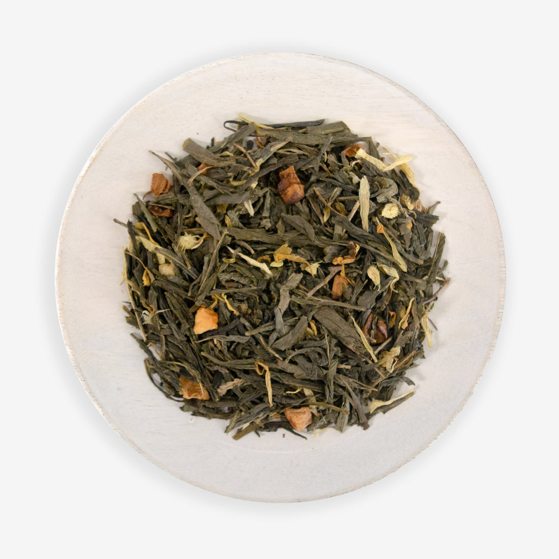 A top view of a bowl containing loose green tea leaves, with pieces of ginger and dried apple, against a white background.