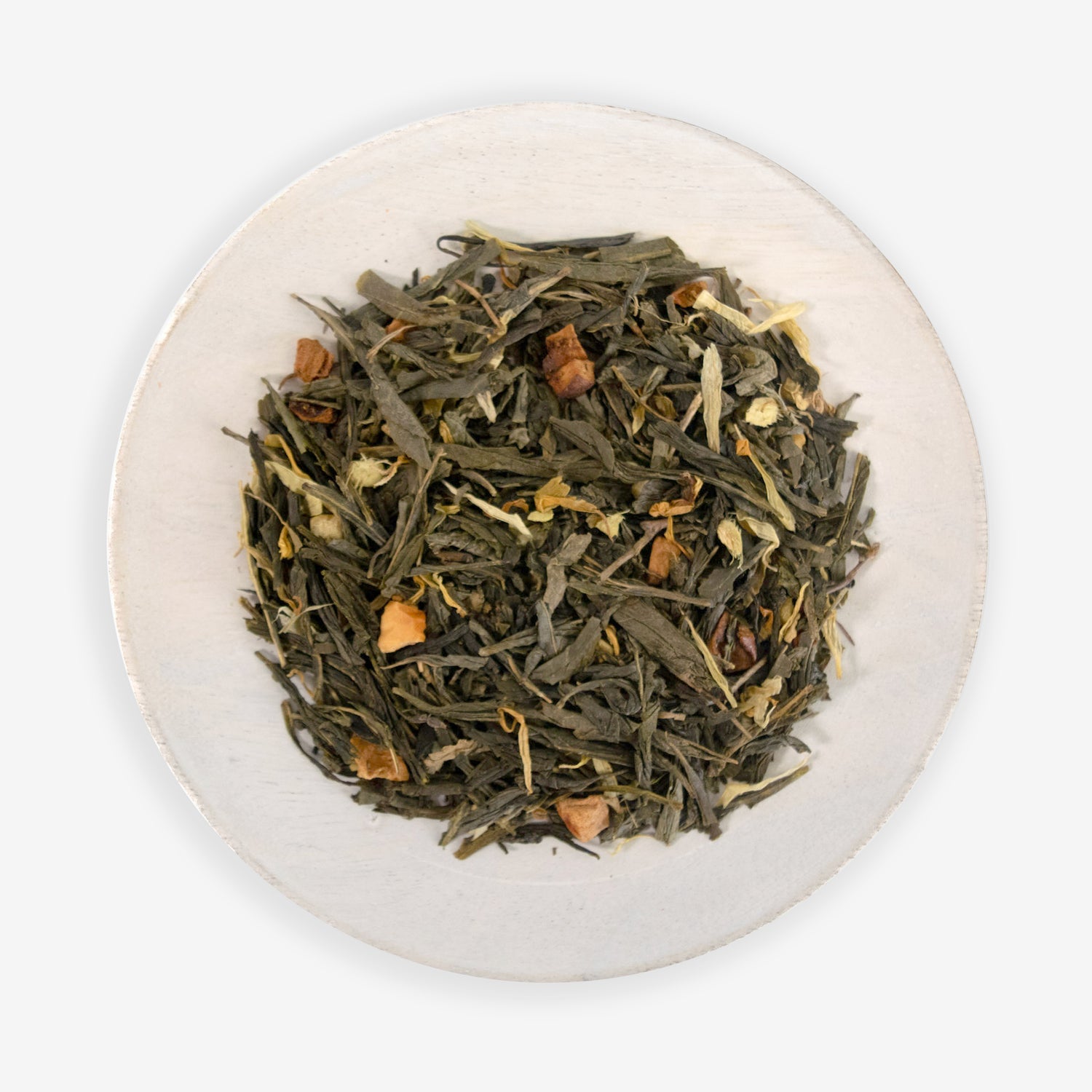 A top view of a bowl containing loose green tea leaves, with pieces of ginger and dried apple, against a white background.