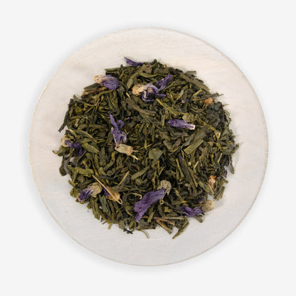 A plate with loose leaf tea that includes green tea buds and purple dragonfruit pieces, along with candied flower petals.