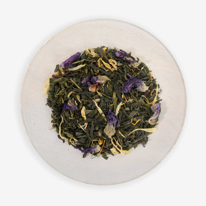 A top view of a plate containing dried tea leaves and pieces of hibiscus flowers, with hints of purple and yellow, on a white background.
