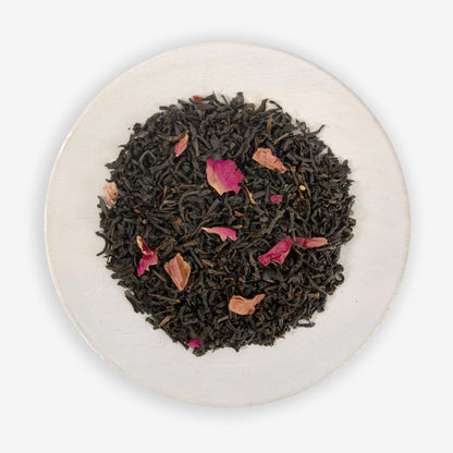A dish containing black tea leaves with pieces of rose petals scattered throughout.