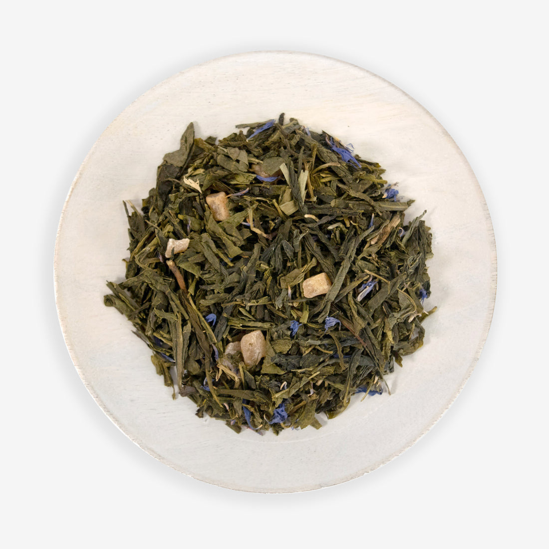 A dish containing green tea leaves, air-dried mango pieces, and blue cornflower petals, indicative of the ingredients in the tea product &