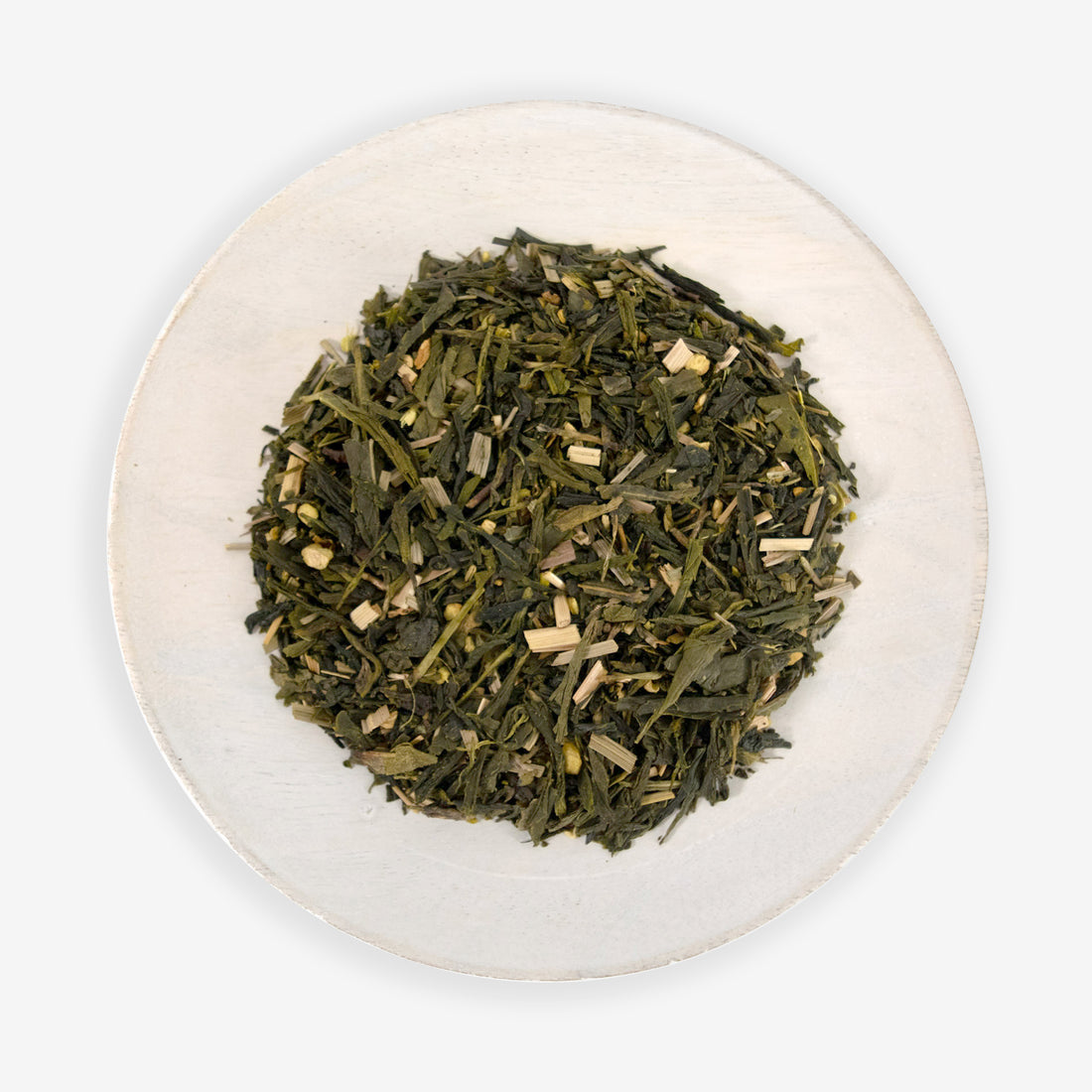 A top view of a plate containing loose leaf green tea mixed with pieces of ginger and lemongrass.