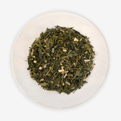 A top view of a plate containing loose leaf green tea mixed with pieces of ginger and lemongrass.