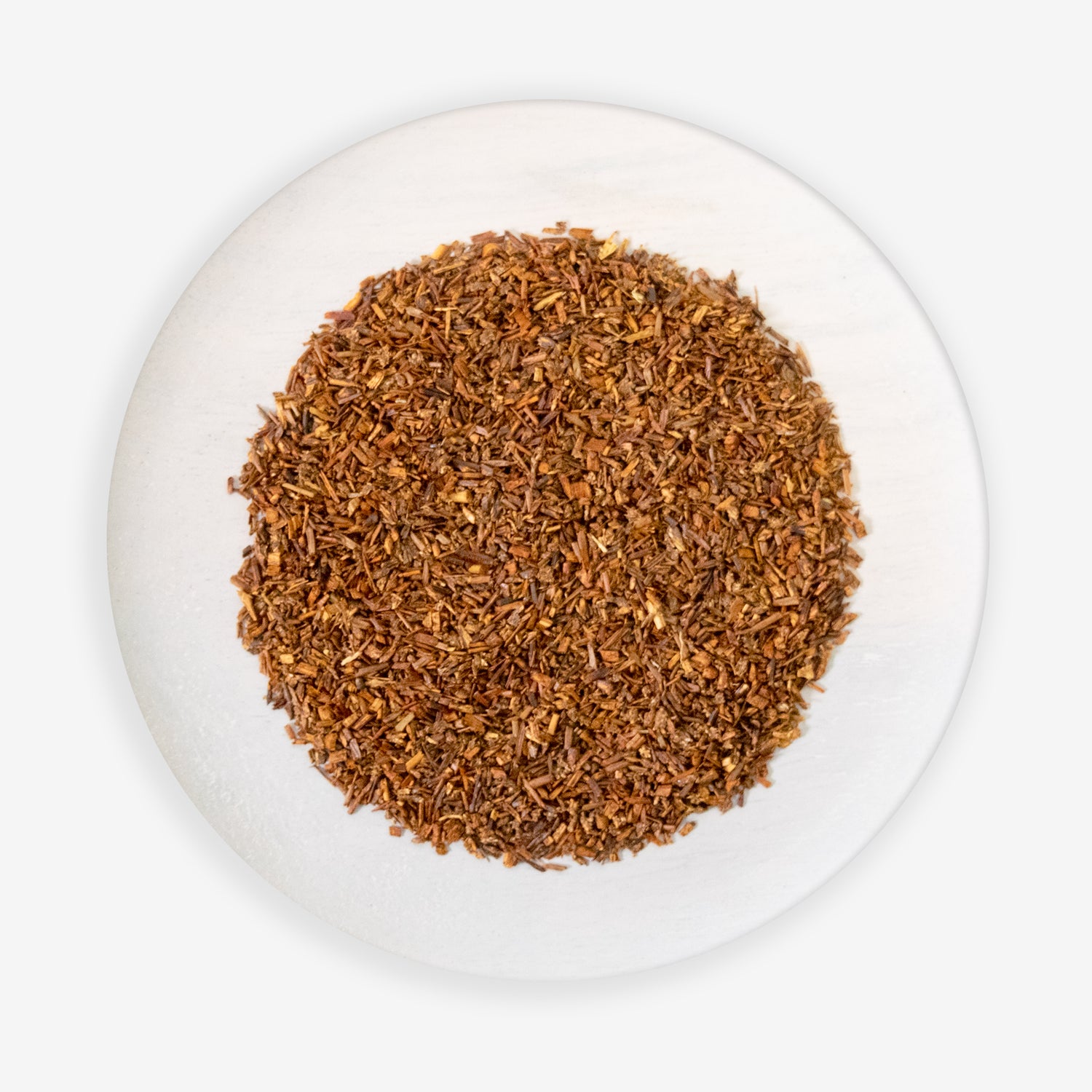 A top view of a plate containing loose red rooibos tea leaves.