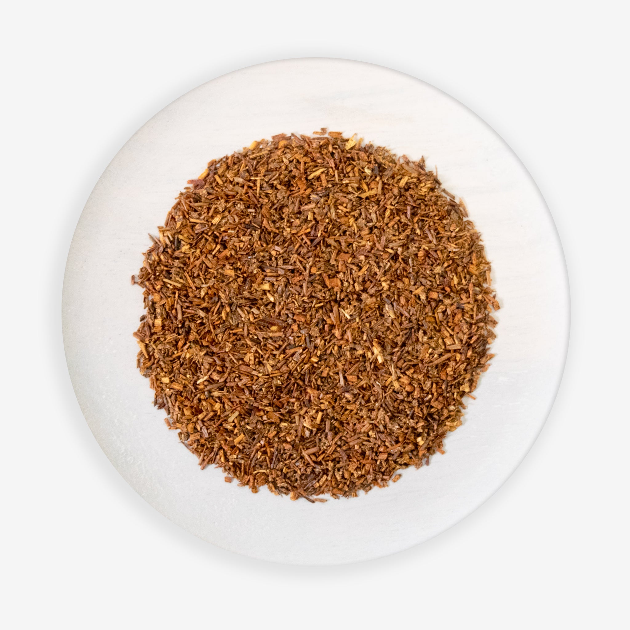 A top view of a plate containing loose red rooibos tea leaves.